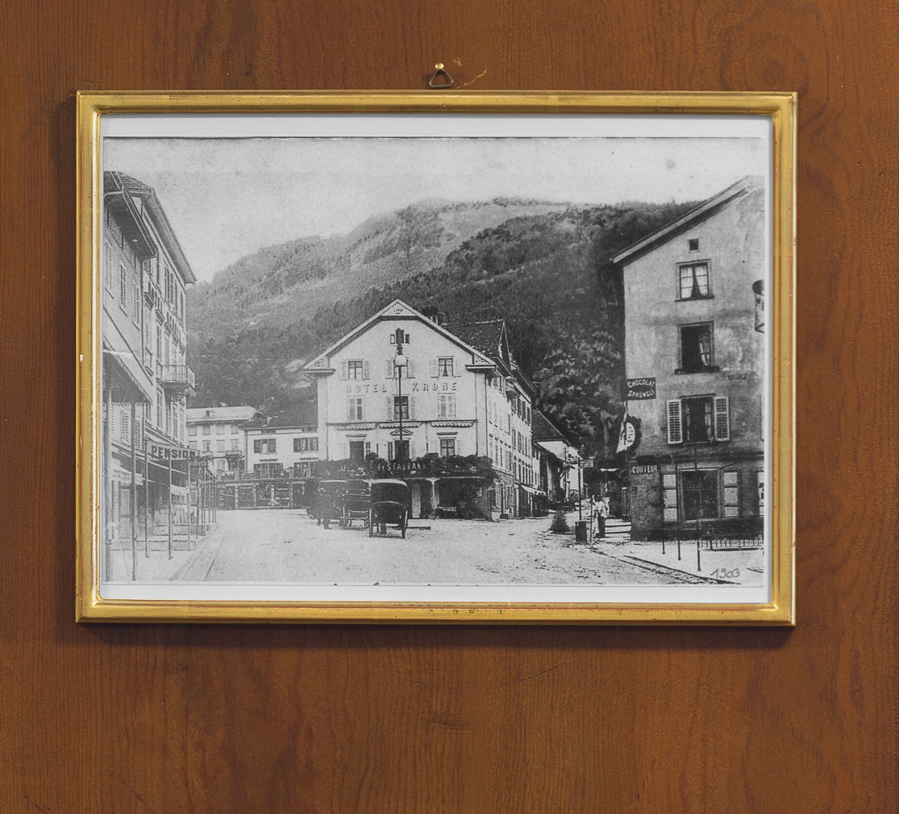 Une photographie en noir et blanc représentant une scène de rue avec des bâtiments, dont un hôtel et un restaurant.
