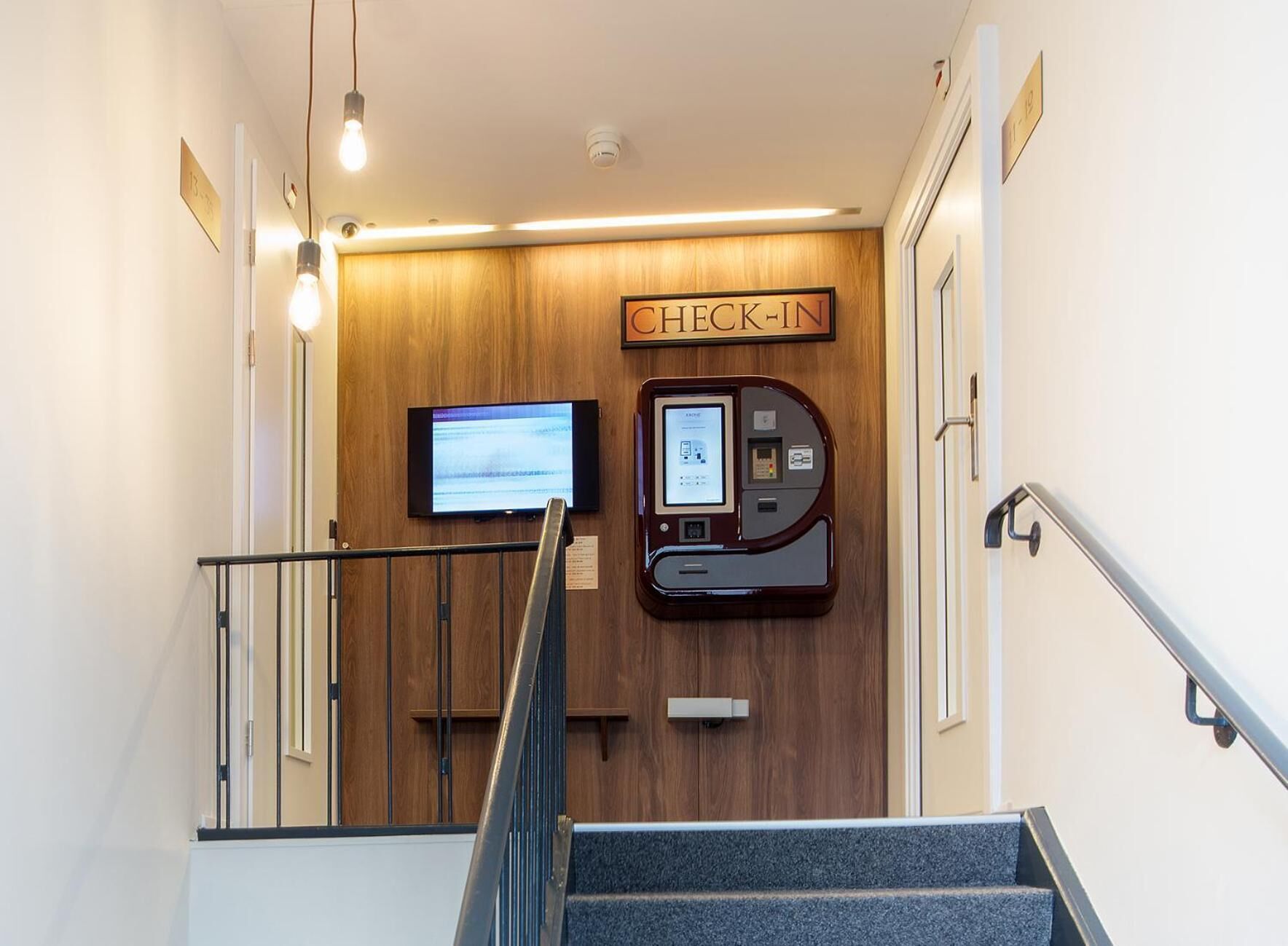 Un espace d’enregistrement doté d’un mur en bois, d’un écran numérique et d’un terminal en libre-service.