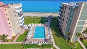 Un hôtel doté d’une piscine centrale entourée de chaises longues, offrant une vue sur la plage et comprenant une pelouse bien entretenue.