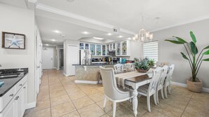A modern kitchen with white cabinets, a central island, and a dining area with white chairs.