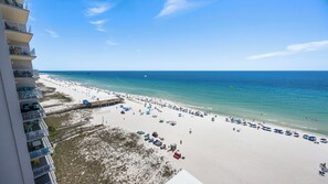 A beach with a pier extending into the ocean, a sandy beach with umbrellas, and a building with balconies overlooking the beach.