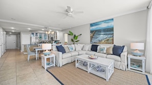 A modern living room with a sectional sofa, two side tables, a coffee table, and a large ocean view painting.