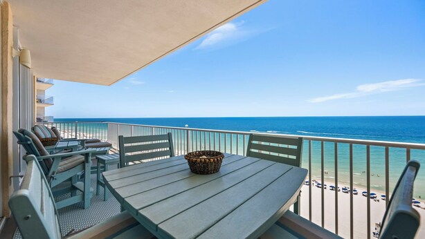Een balkon met een tafel en stoelen, een rieten mand en uitzicht op het strand en de oceaan.