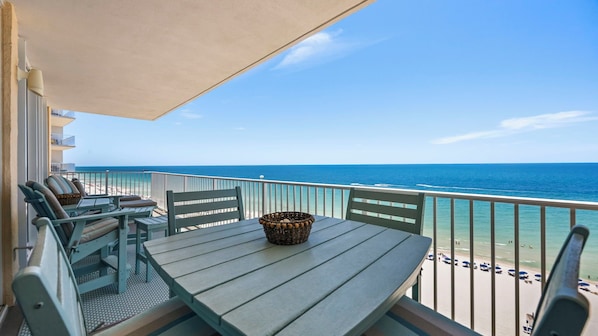 A balcony with a table and chairs, a wicker basket, and a view of the beach and ocean.