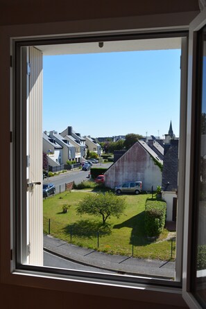 A residential street view through a window, featuring houses, a small green area, and a parked vehicle.