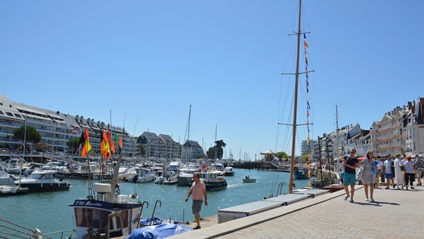 Un port de plaisance avec des bateaux amarrés, un ciel dégagé et des bâtiments le long de la promenade.