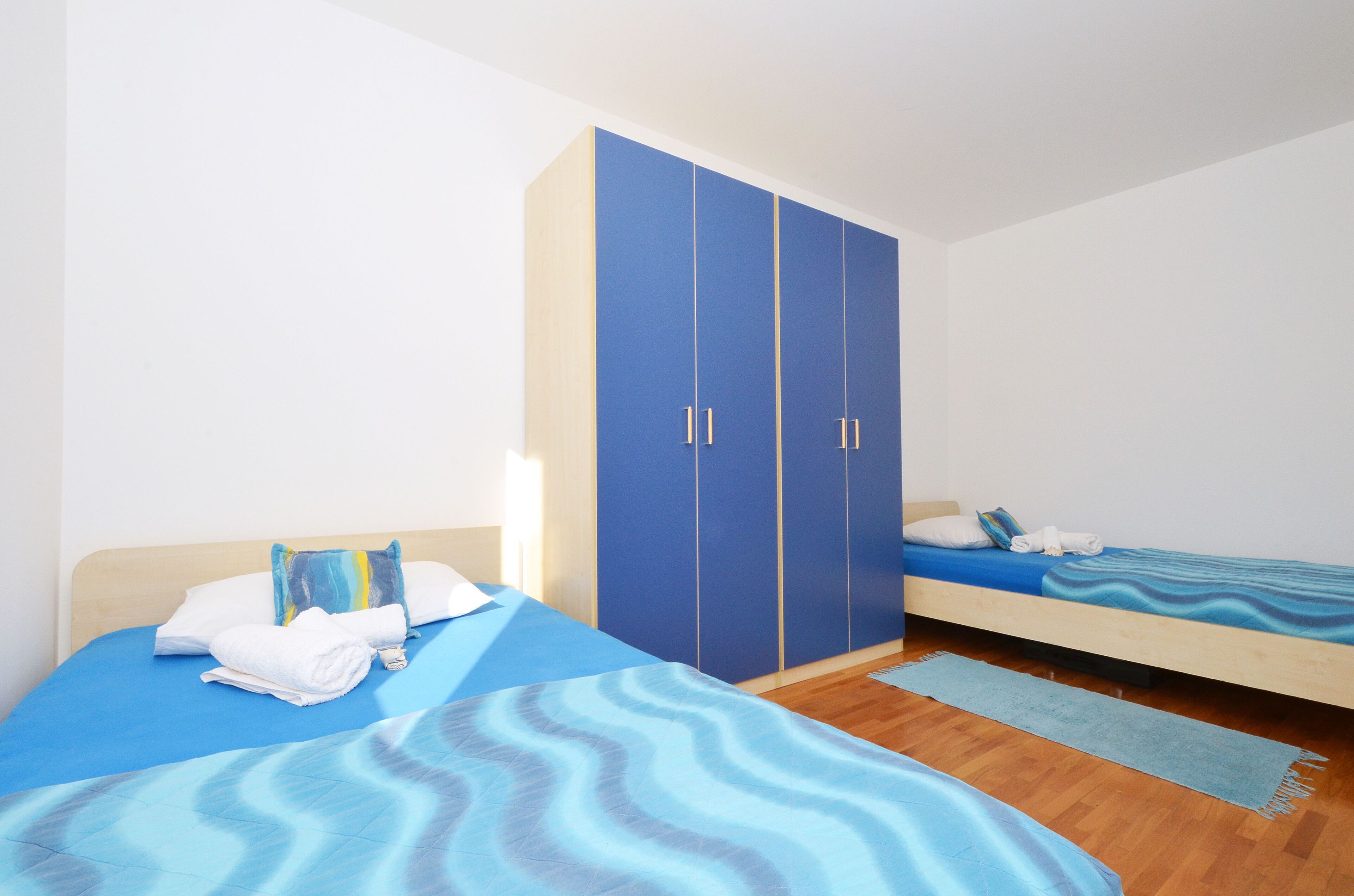 A bedroom with two beds, a wardrobe, and a blue patterned bedspread.