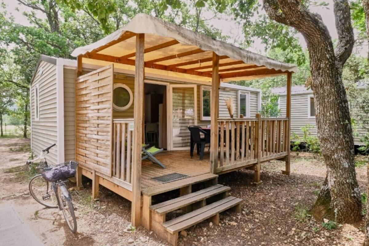 A wooden deck with a covered porch, a bicycle, and a tree in the background.