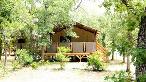 A rustic cabin with a porch, surrounded by trees. - Domaine des Chênes Blancs - Camping (Saint-Saturnin-les-Apt)