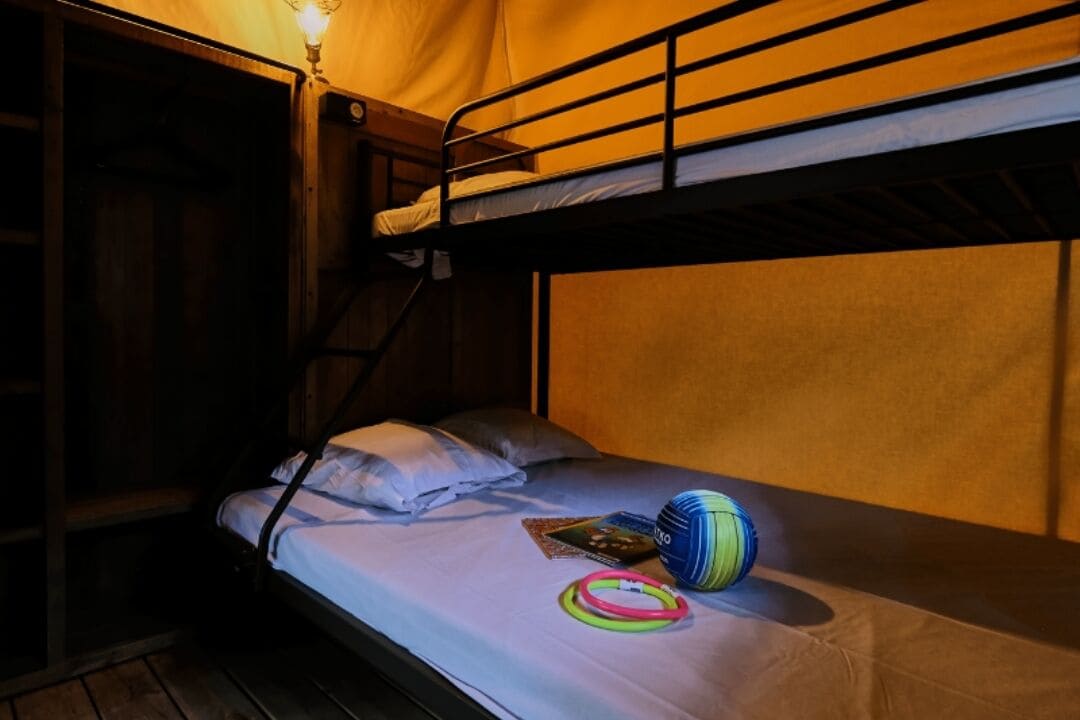 A bunk bed room with a single bed on the lower bunk, a light fixture above, and a ball and rings on the bed.