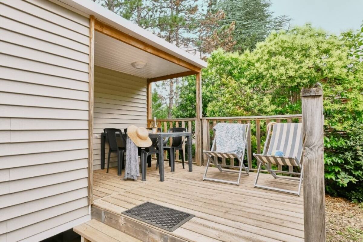 A covered outdoor deck with a table and chairs, surrounded by greenery.