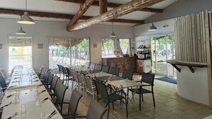 A long dining table with chairs, wooden beams on the ceiling, and a coffee machine in the background. - Domaine des Chênes Blancs - Camping (Saint-Saturnin-les-Apt)