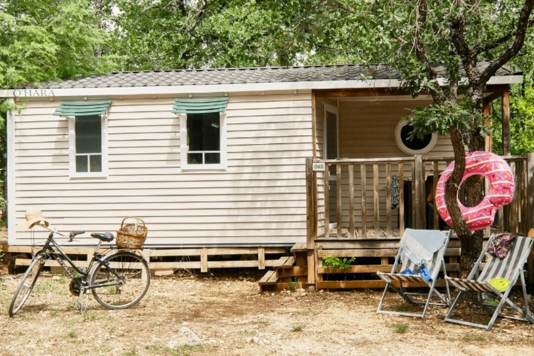 Une petite cabane à un seul étage, dotée d’une véranda, d’un vélo et de chaises de plage.