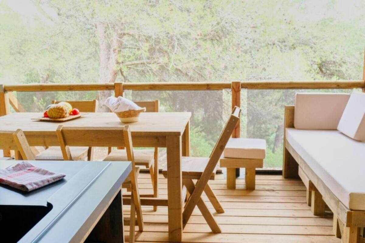 A wooden deck with a table and chairs, a bench, and a view of trees.