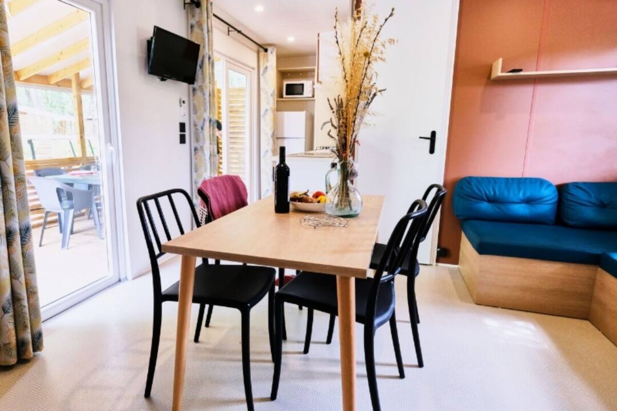 A dining area with a wooden table, black chairs, a vase with dried plants, and a blue sofa.