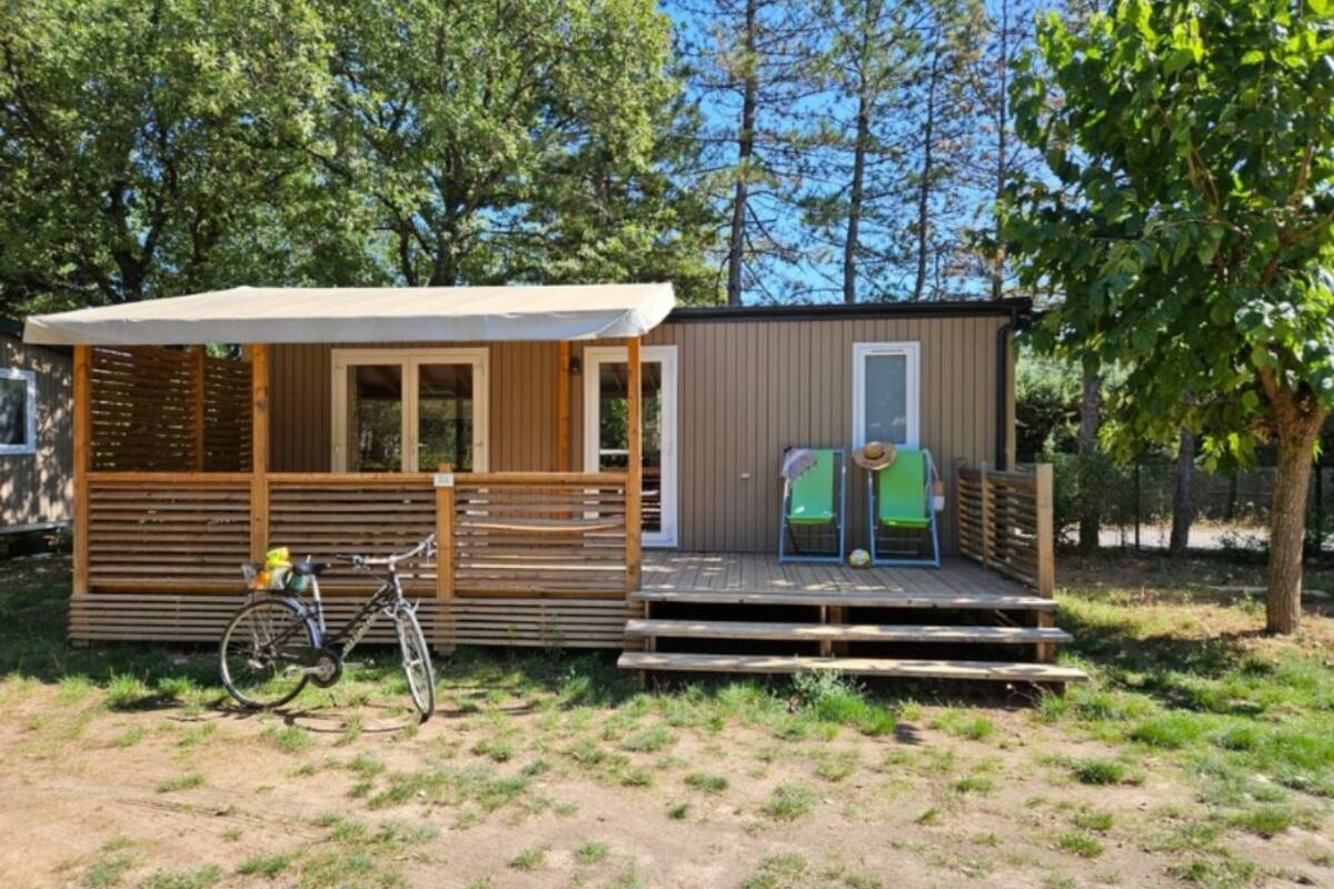 A small wooden cabin with a porch, a bicycle, and a door with a hat hanging on it.