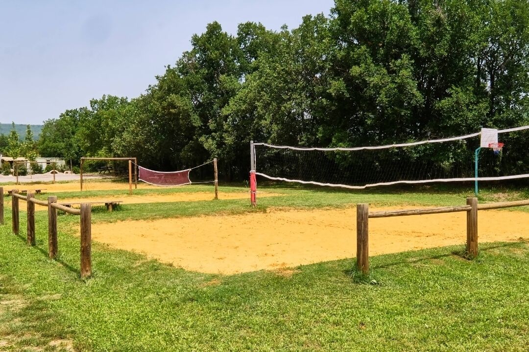A volleyball court with a net, surrounded by a wooden fence and a grassy area.