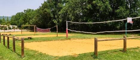 A volleyball court with a net, surrounded by a wooden fence and a grassy area.