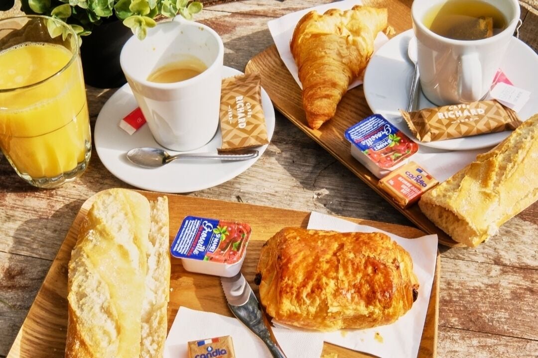 A breakfast setting with croissants, coffee, and juice on a wooden table.