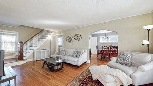 A spacious living room with a staircase, white sofas, a coffee table, and a dining area with a chandelier. - Belltown Retreat - Shopping, Dining, Pet Friendly (Stamford)