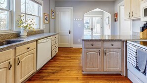 A kitchen with wooden cabinets, a granite countertop, and a view of the backyard through an archway. - Belltown Retreat - Shopping, Dining, Pet Friendly (Stamford)
