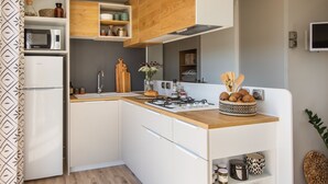A modern kitchen with white cabinetry, a wooden countertop, and a built-in microwave. - Camping Pascalounet (Martigues)