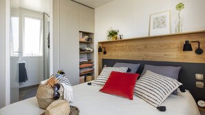 A bedroom with a bed, bedside tables, a wooden headboard, a shelf with decorative items, and a wardrobe. - Camping Pascalounet (Martigues)