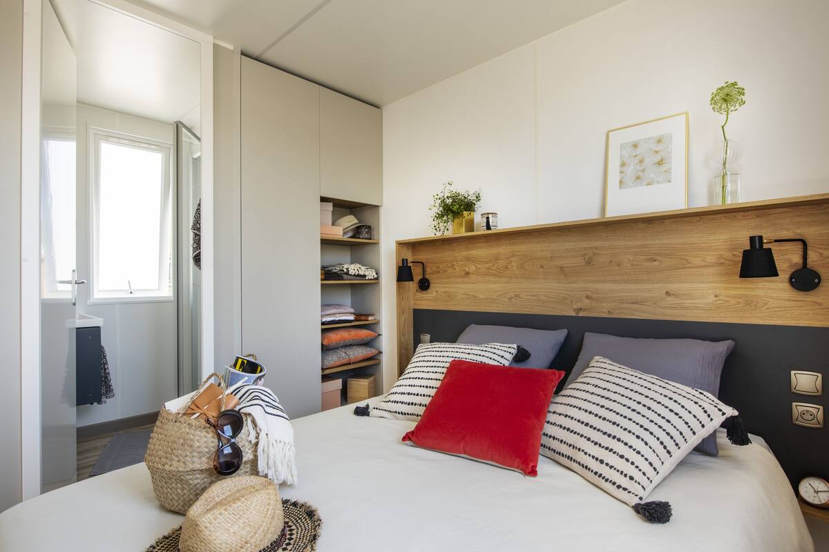 Une chambre à coucher comprenant un lit, des tables de chevet, une tête de lit en bois, une étagère avec des objets décoratifs et une armoire.