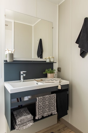 Un baño moderno con un lavamanos blanco, un mueble oscuro y un espejo encima.