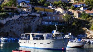 A coastal town with boats docked at the harbor, houses on a hillside, and a rocky cliff. - Camping Pascalounet (Martigues)