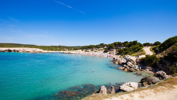 A coastal beach with clear turquoise waters, rocky shoreline, and a path leading to the beach. - Camping Pascalounet (Martigues)