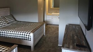 A bedroom with a bed, a nightstand, a TV, and a bathroom with a sink and mirror. - Eden Getaway (Eden)