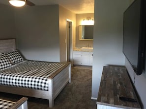 A bedroom with a bed, a nightstand, a TV, and a bathroom with a sink and mirror. - Eden Getaway (Eden)