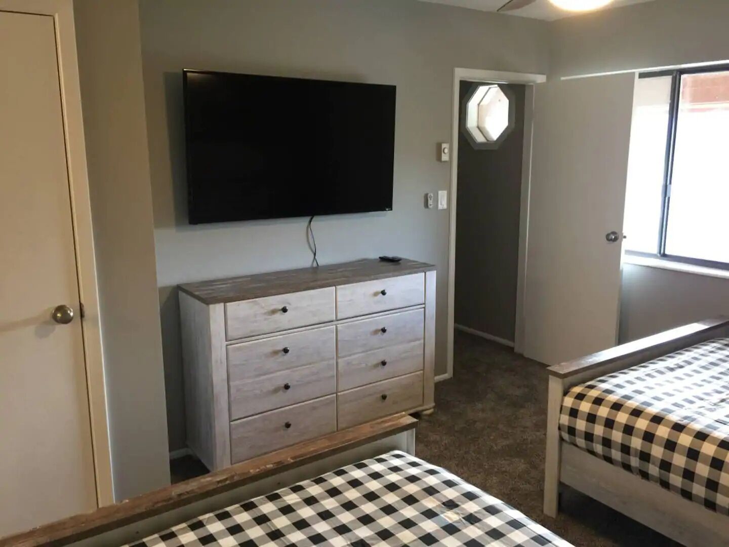 Une chambre à coucher avec un lit, une commode, un téléviseur fixé au mur et une fenêtre.