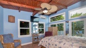 A bedroom with a bed, a chair, a ceiling fan, and large windows.