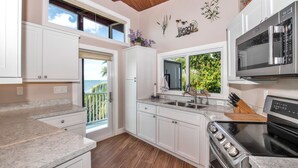 A modern kitchen with white cabinetry, a stainless steel stove, and a large window overlooking greenery.