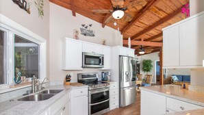 A kitchen with white cabinets, stainless steel appliances, a wooden ceiling, and a view into the living area.