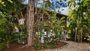 A rustic wooden house surrounded by lush greenery and a gravel path.