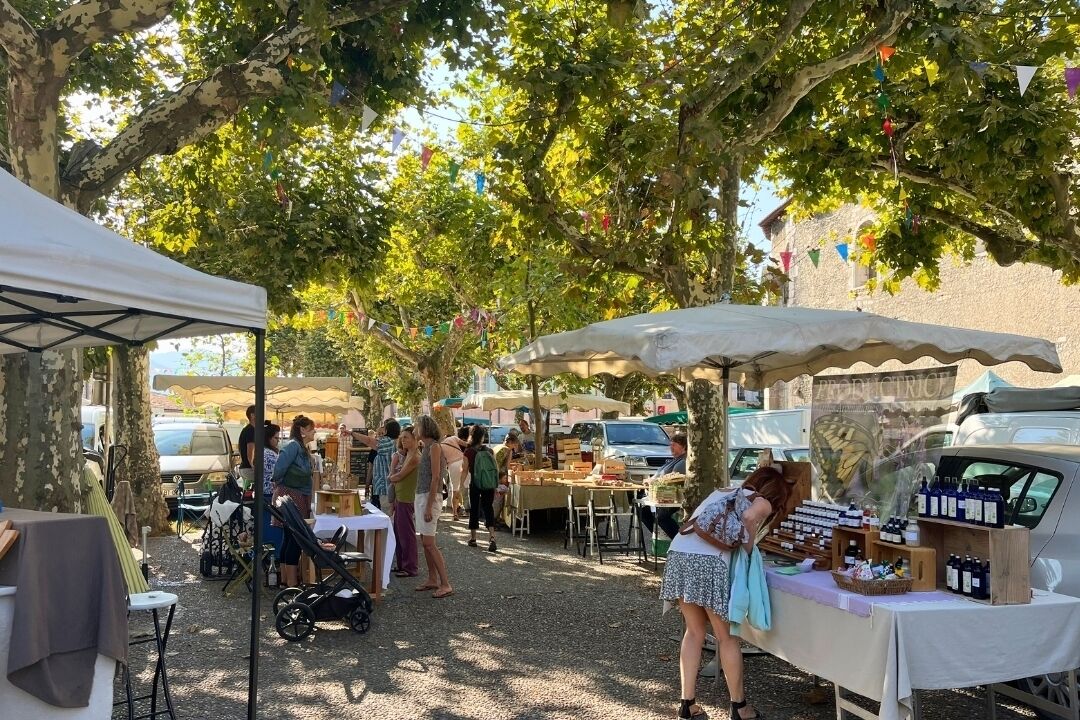 Mercado al aire libre con mesas y carpas bajo árboles.