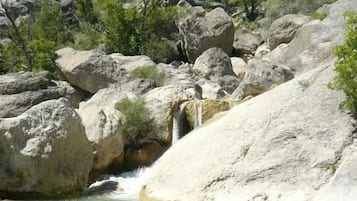 A natural landscape with a waterfall, rocky terrain, and sparse vegetation.