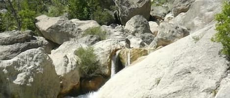 A natural landscape with a waterfall, rocky terrain, and sparse vegetation.