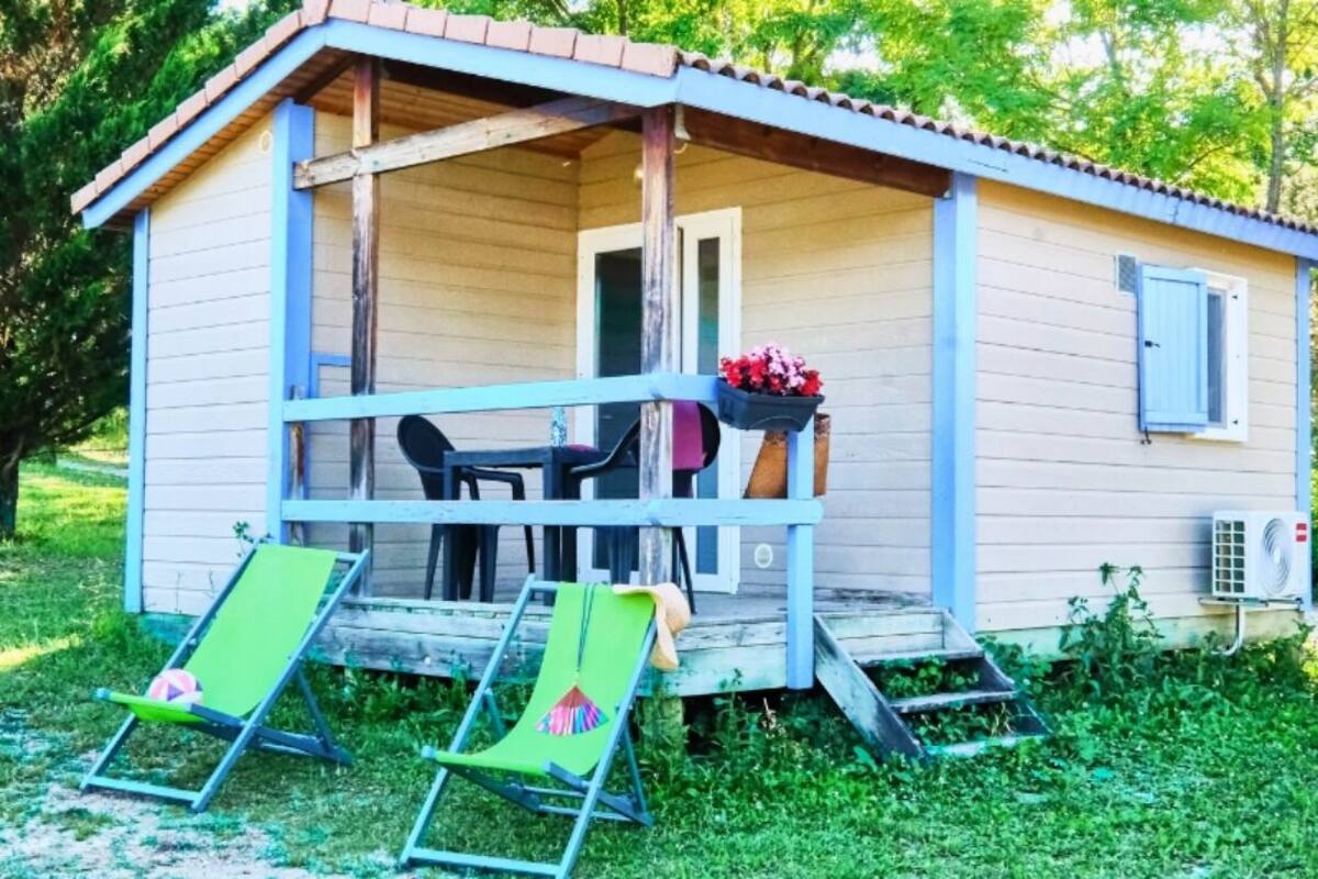 Eine kleine Holzhütte mit Veranda, zwei grüne Liegestühle, einem Tisch und einem hängenden Blumentopf.