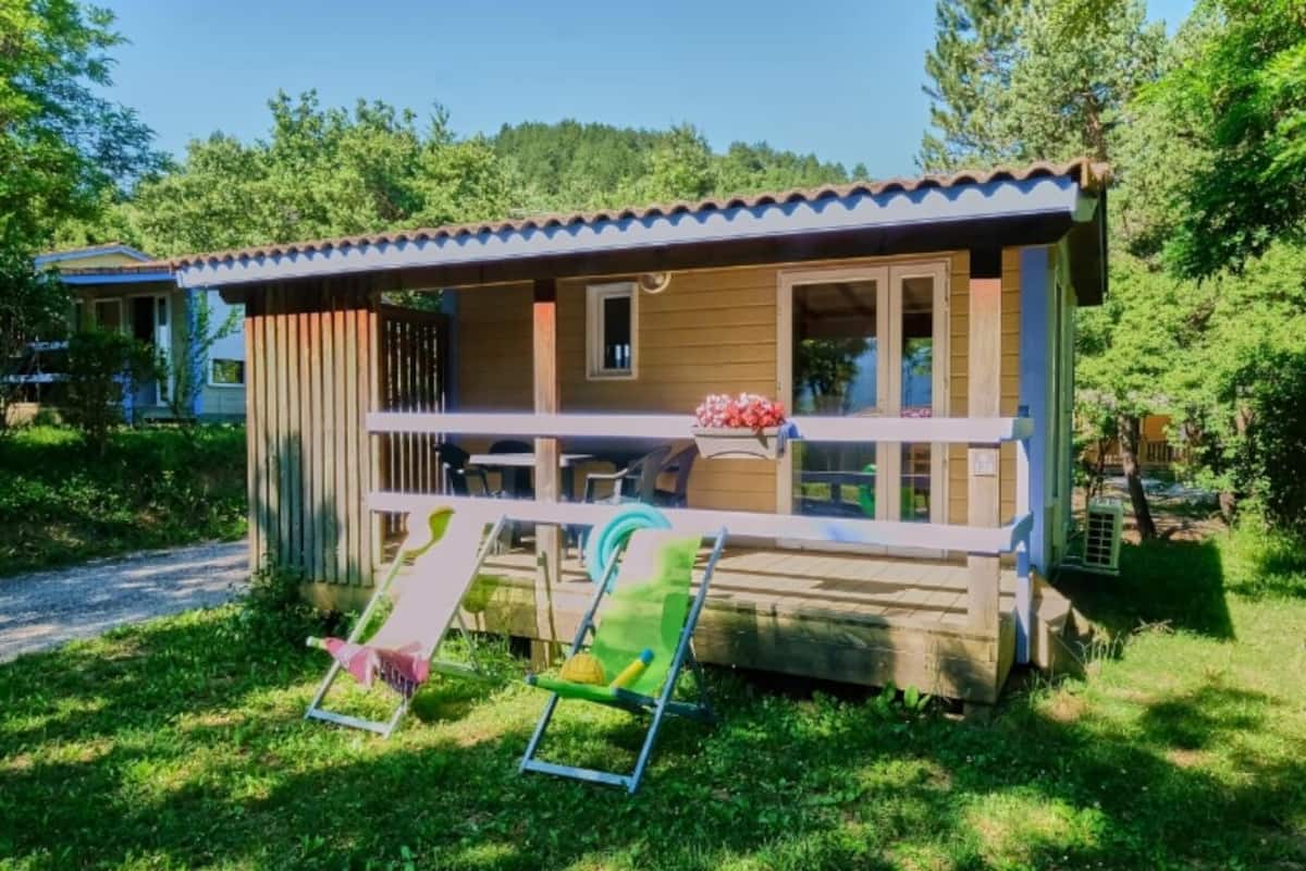Ein kleines Holzhaus mit einer Veranda, einer Rutsche und einem grünen Stuhl.