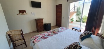 Un dormitorio con cama, cómoda, silla, televisor y puerta corrediza de vidrio al exterior.