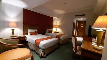 A hotel room with two beds, a desk, a chair, and a nightstand.