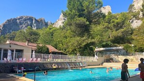 Piscina com pessoas, cercada por árvores e montanhas.