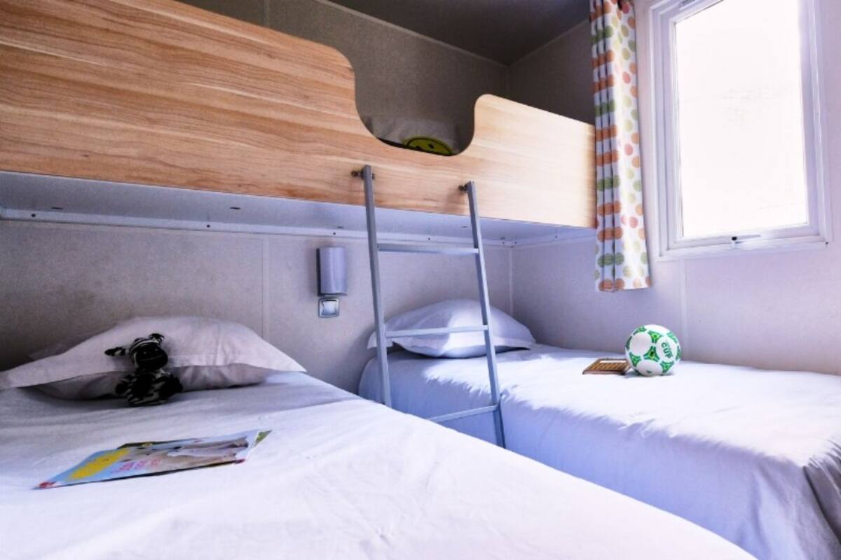 A bunk bed room with a wooden headboard, a window with a curtain, and a soccer ball on one bed.