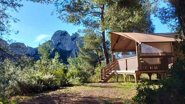 Uma cabana de madeira com varanda coberta e escadaria, cercada por árvores e montanhas.