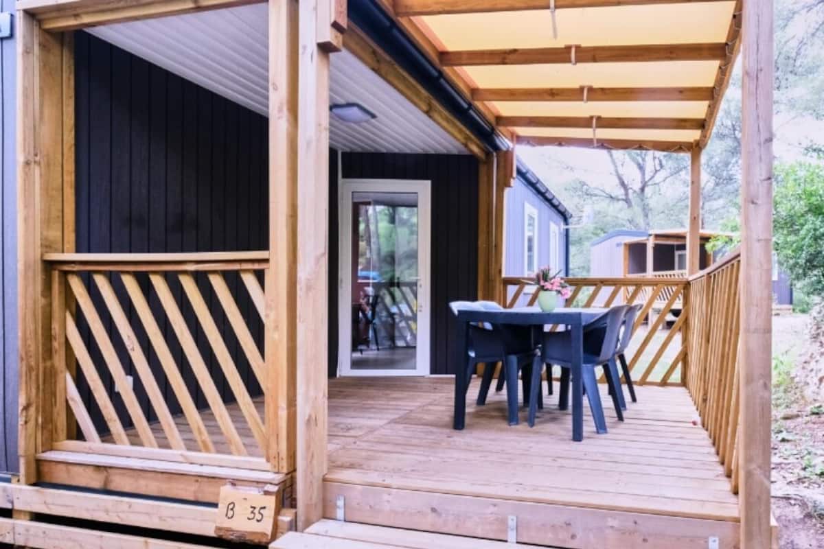 A wooden deck with a table and chairs, a wooden railing, and a door leading to a covered area.