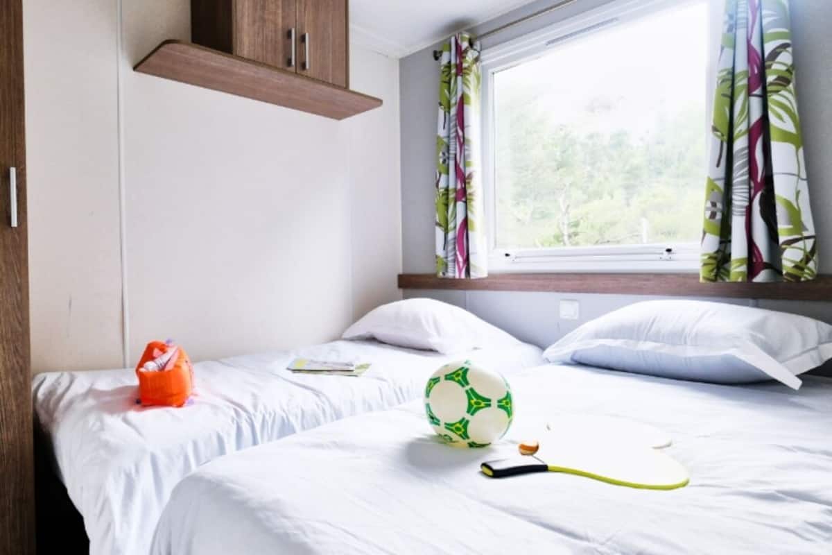 A bedroom with two beds, a window with curtains, a wooden cabinet, and a soccer ball.